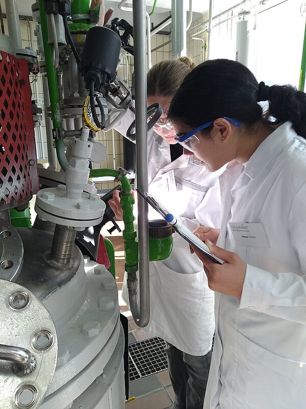 Forschungsteam analysiert technische Apparatur im Labor. Zwei Personen in Laborkitteln arbeiten an einer Maschine.